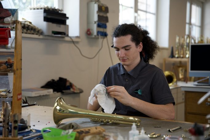 Ein Mann putzt ein Blechblasinstrument in einer Werkstatt.